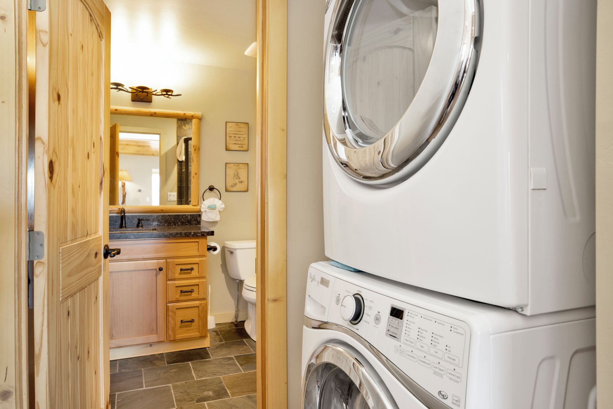 A laundry room with stacked washers and dryers, wooden cabinets, a mirror, and a tiled floor.