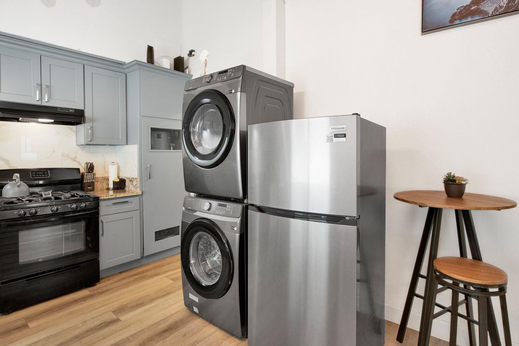 A compact kitchen with a built-in washer and dryer, a stainless steel refrigerator, and a small wooden table with a chair.