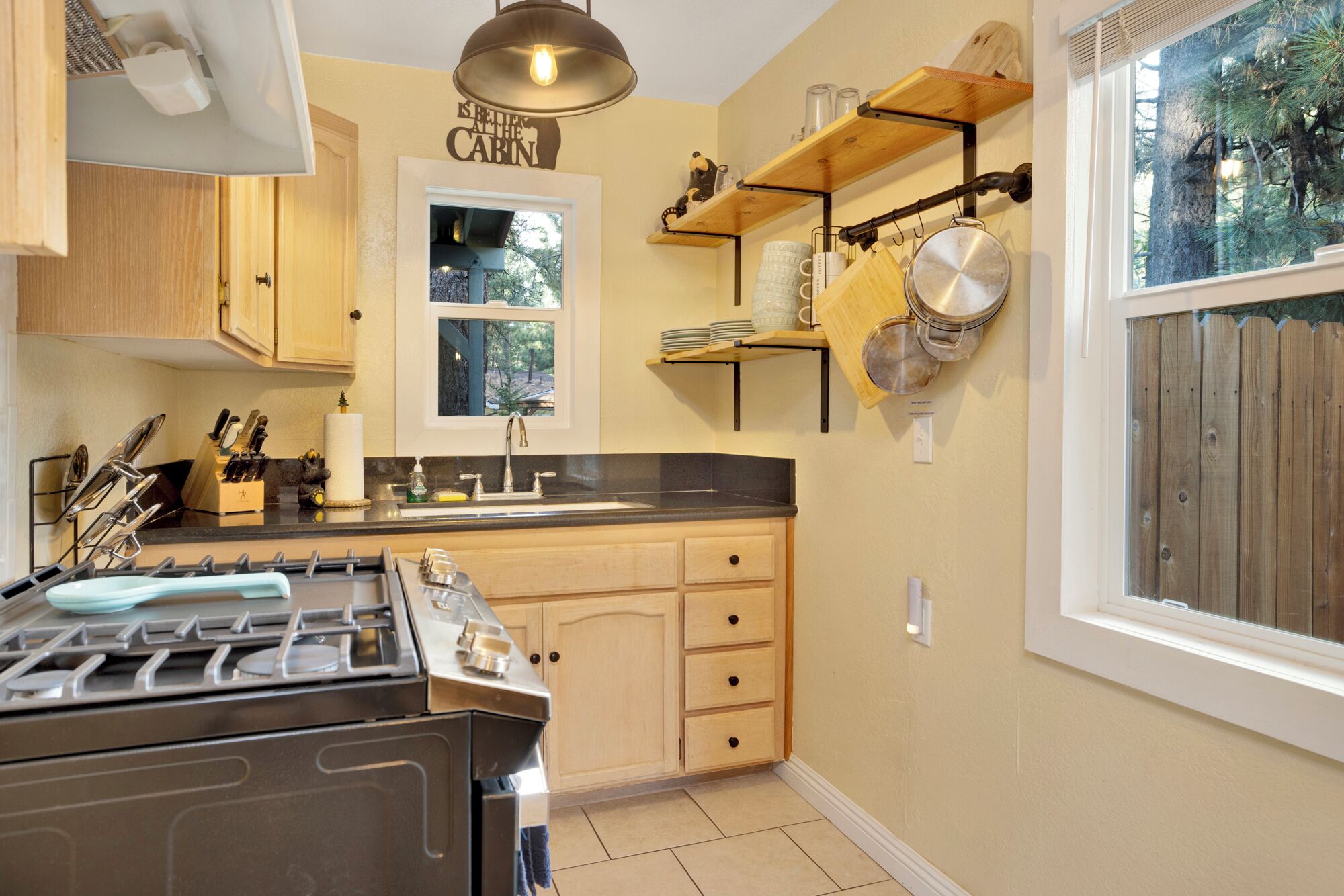 A kitchen with a gas stove, wooden cabinets, a window, and a shelf with cookware.