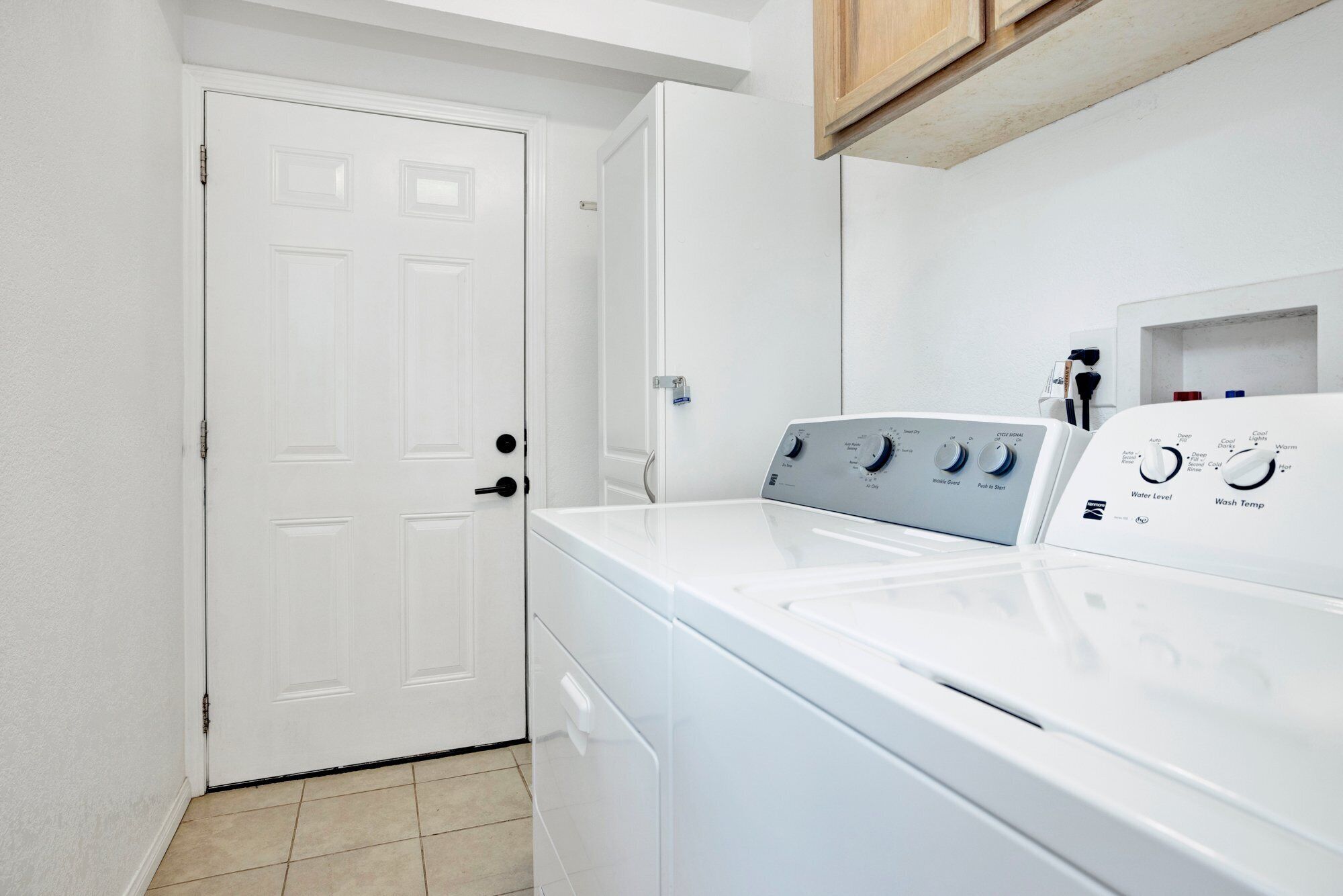 A laundry room with a front-loading washer and dryer, a white door, and a tiled floor.