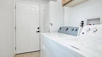 A laundry room with a front-loading washer and dryer, a white door, and a tiled floor.