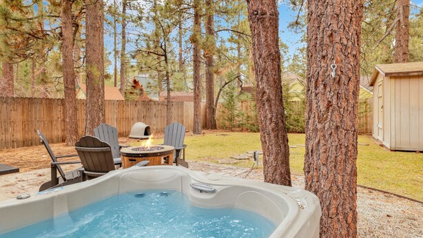 En bubbelpool i en trädgård, med ett trädäck, två Adirondack-stolar och en grill.