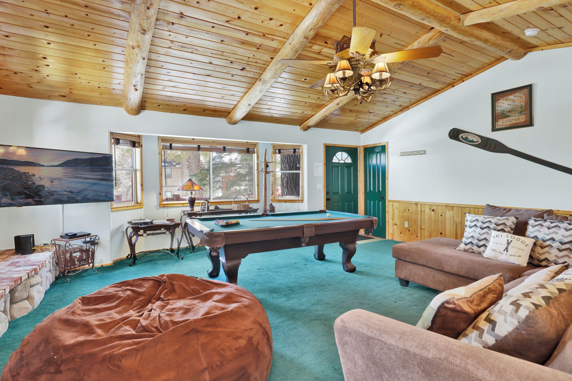 A cozy room with a pool table, comfortable seating, a large window with a view, and a wooden ceiling.