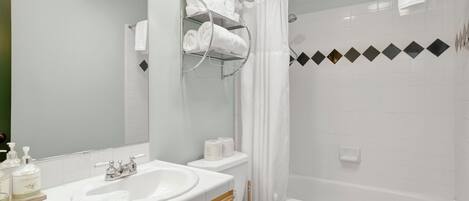 A modern bathroom with a white sink, vanity, and toilet, a glass shower enclosure, and a mirror with a towel rack.