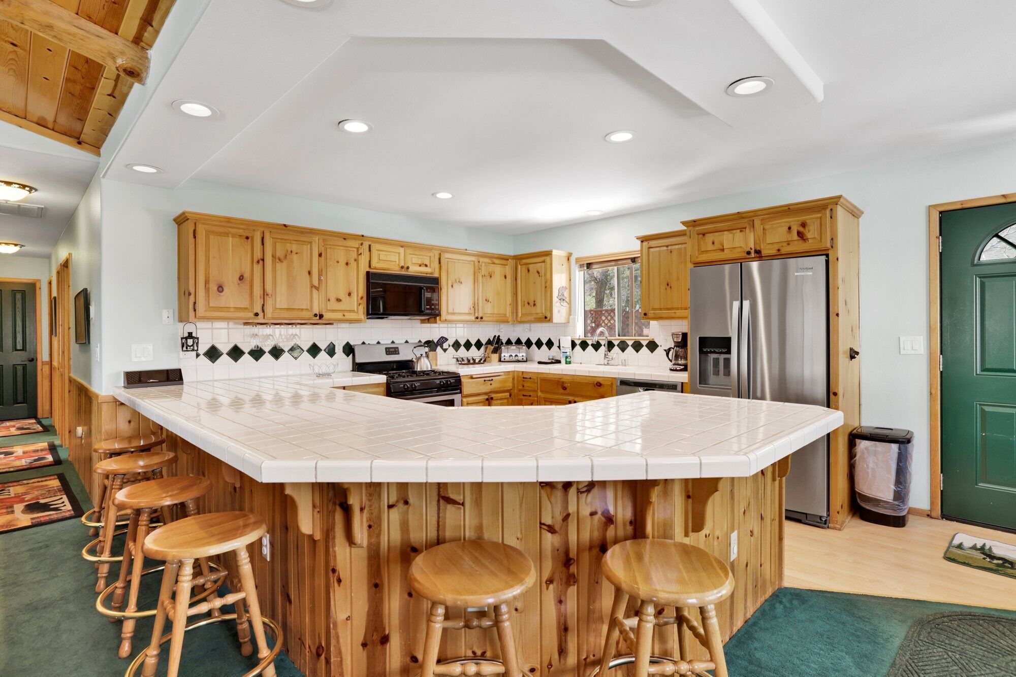 Une cuisine avec des meubles en bois, un grand îlot central doté de tabourets, un réfrigérateur en acier inoxydable et un four à micro-ondes.