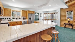 A spacious kitchen with wooden cabinets, a stainless steel refrigerator, and a large island with stools. - Alameda Landing #2345 (Big Bear City)