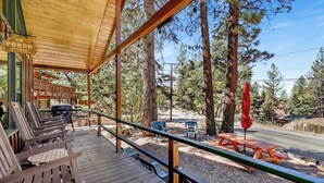 Une terrasse en bois avec des sièges d’extérieur, un barbecue et une vue sur une zone boisée.