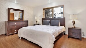 A bedroom with a bed, two bedside tables, a dresser, a large mirror, and a window with a view of buildings. - THE Octagon #2394 (Big Bear City)