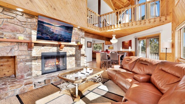 A spacious living room with a stone fireplace, leather sofa, and a high wooden ceiling. - THE Octagon #2394 (Big Bear City)