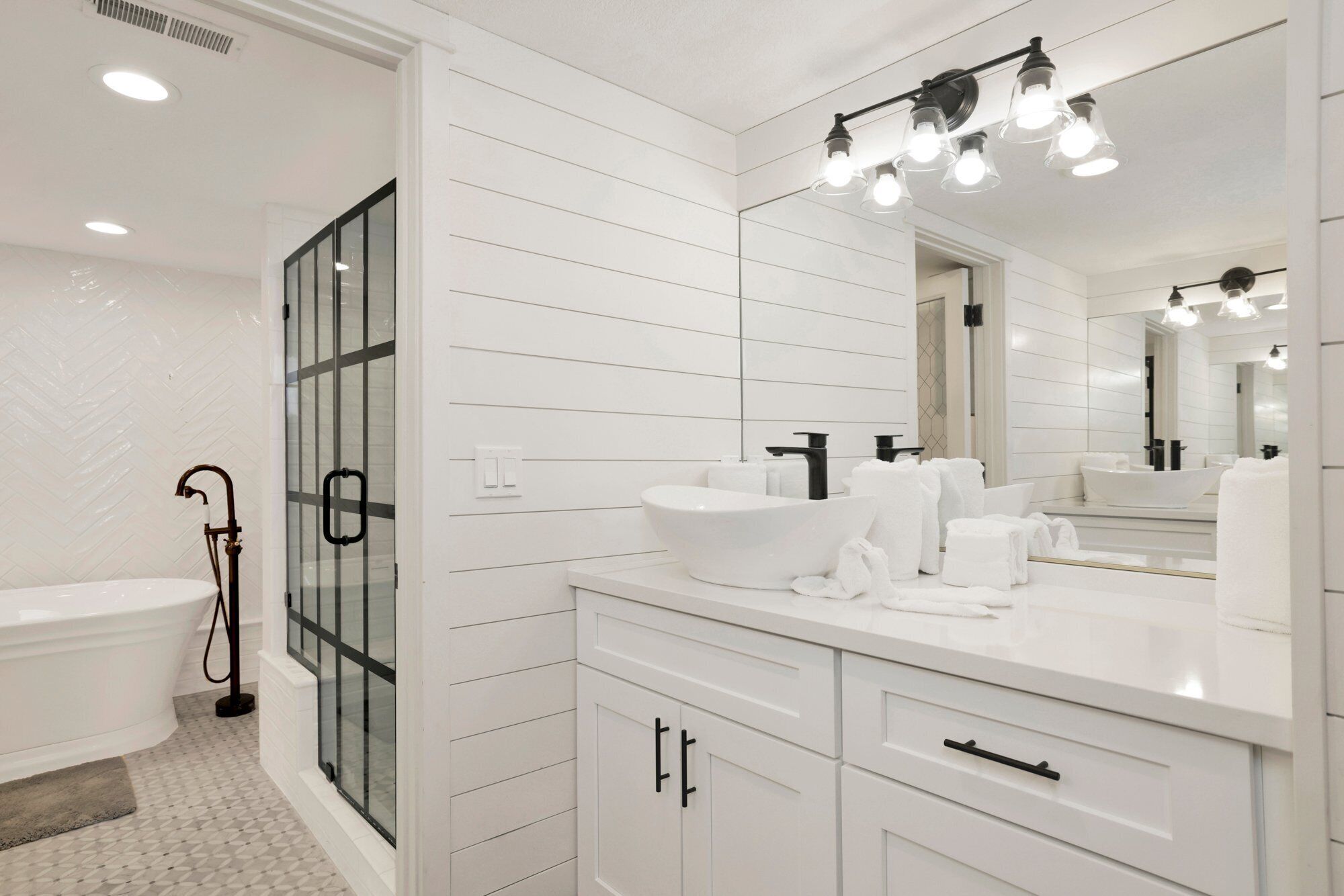 A modern bathroom with a freestanding bathtub, a large mirror, and a vanity with a sink and towel rack.
