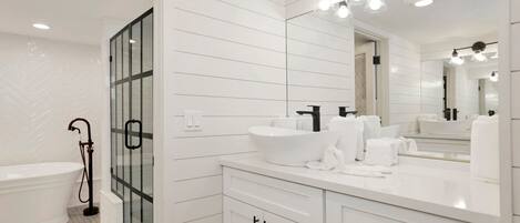 A modern bathroom with a freestanding bathtub, a large mirror, and a vanity with a sink and towel rack.