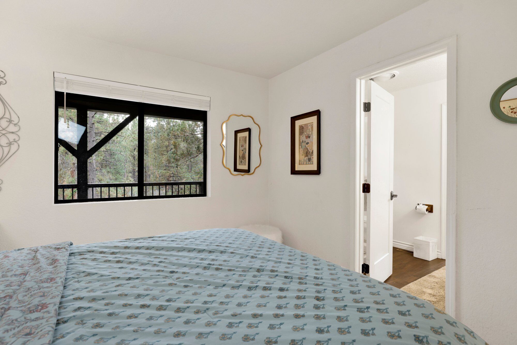 A bedroom with a bed, a window with a black frame, and a door leading to another room.