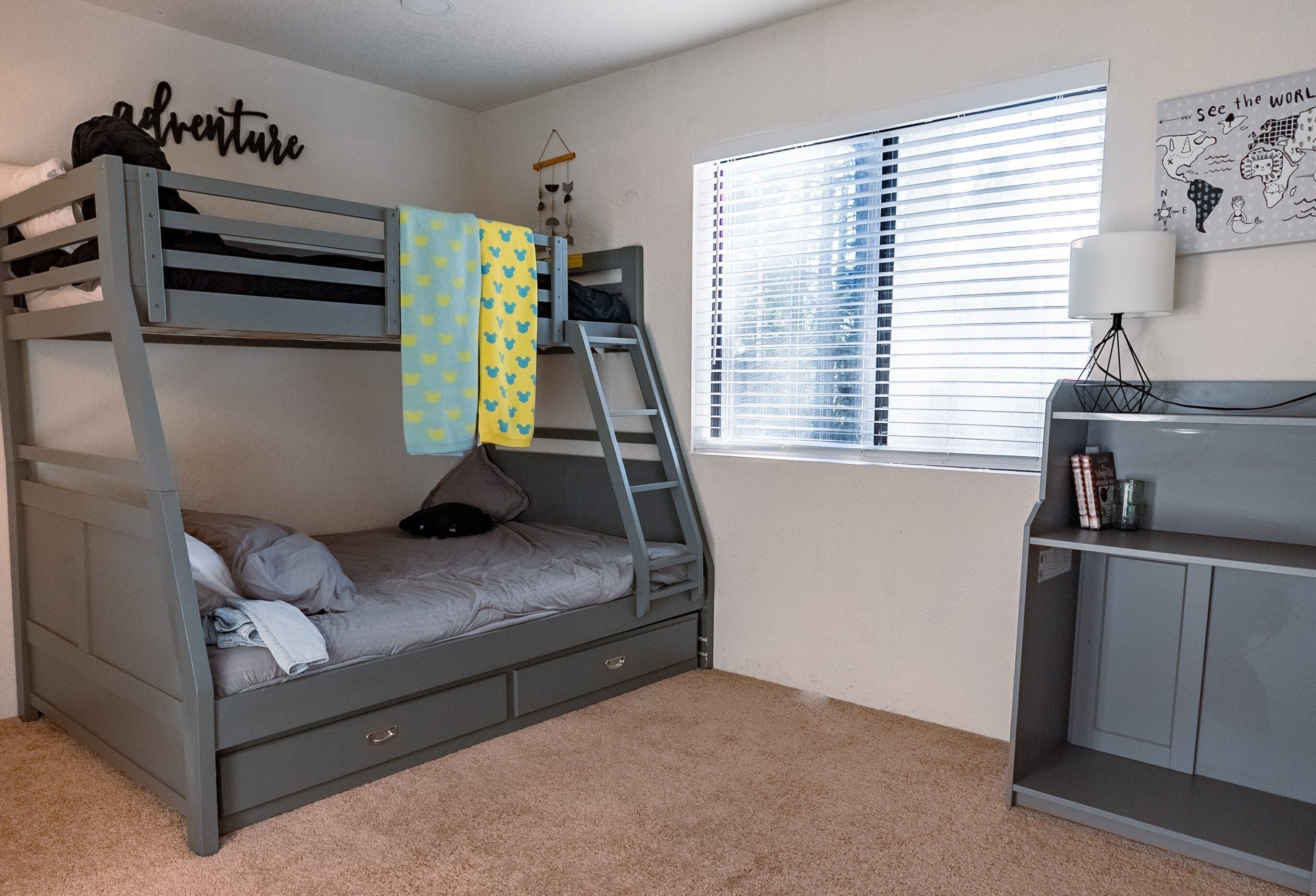 A bunk bed with a ladder, a desk with a lamp, and a world map on the wall.