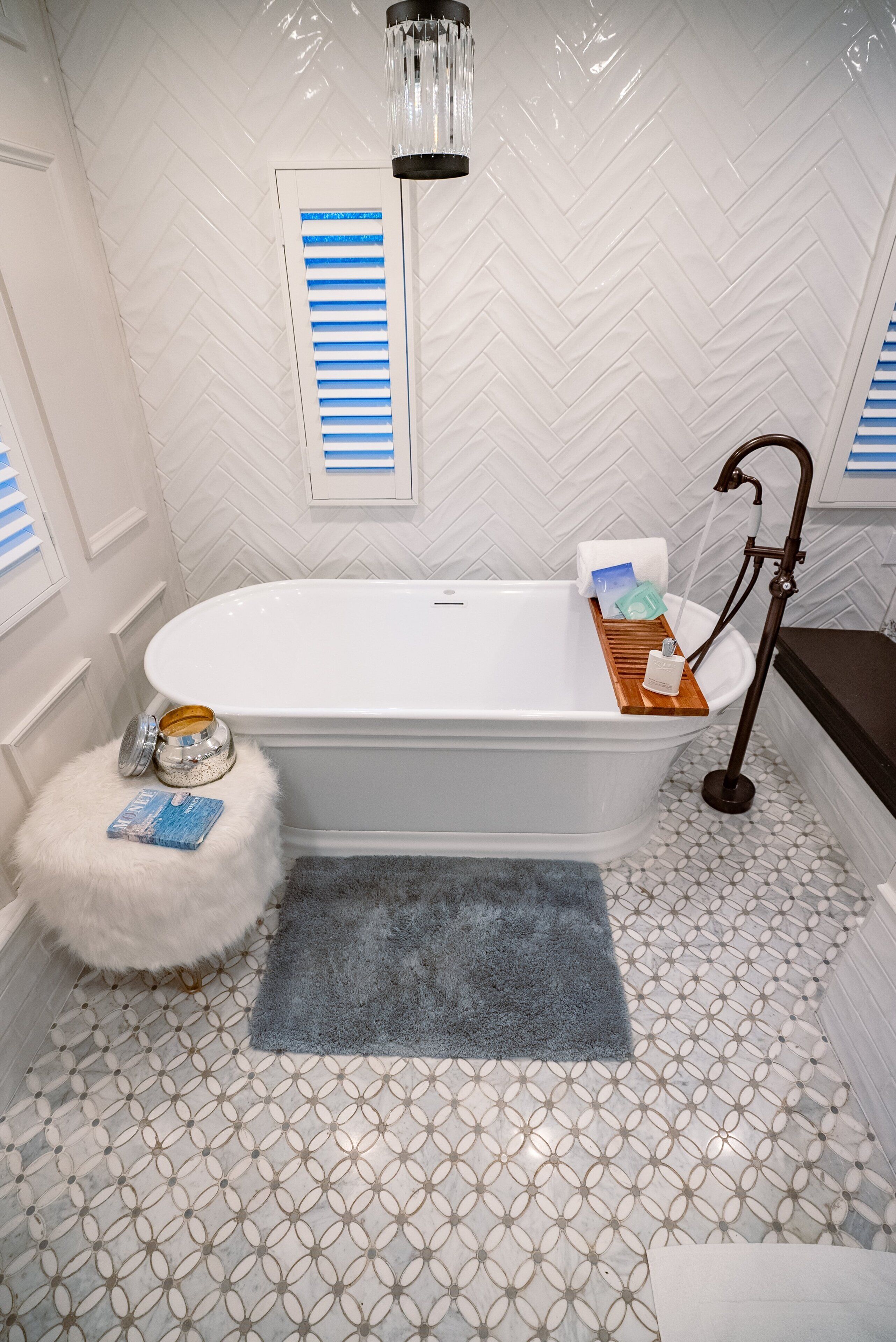 A bathroom with a freestanding bathtub, a wooden tray, a fluffy stool, and a blue rug.