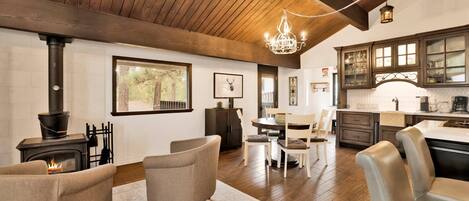 A spacious living area with a fireplace, comfortable seating, a dining table, and a kitchen with dark wooden cabinets.