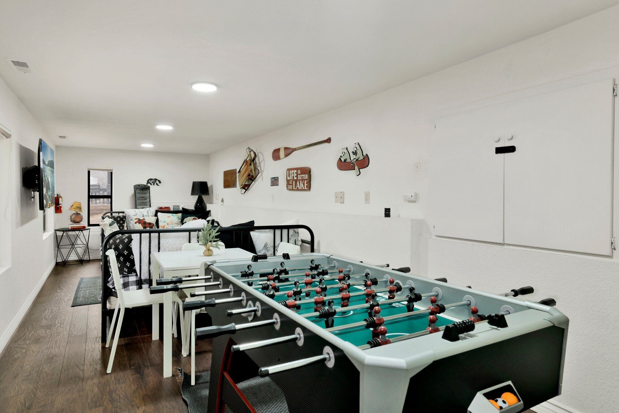 A room with a foosball table, a bed, a desk, and a window.