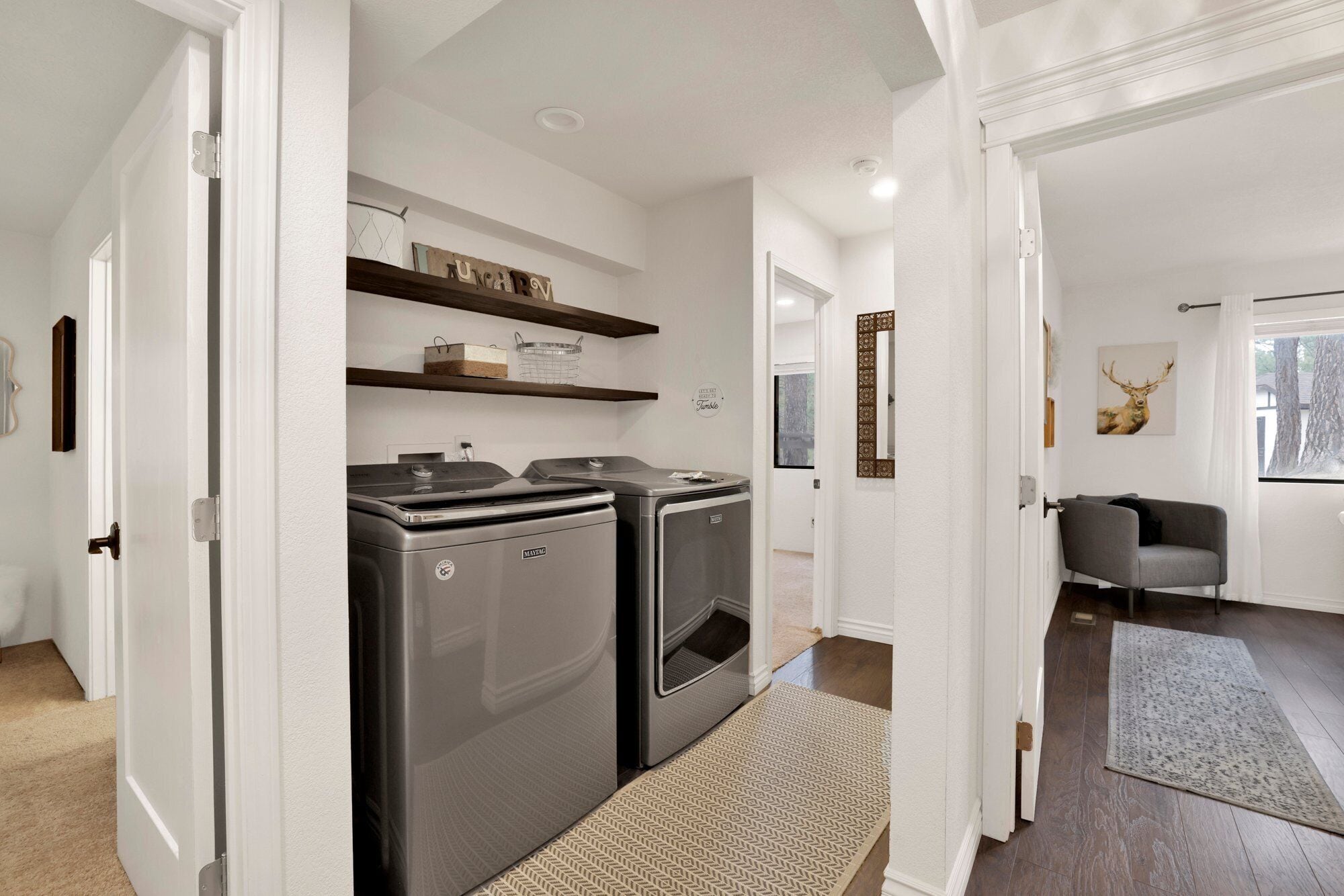 Een moderne keuken met twee Maytag wasmachines, een houten plank erboven en een zithoek met een grijze bank en een schilderij van een hert.