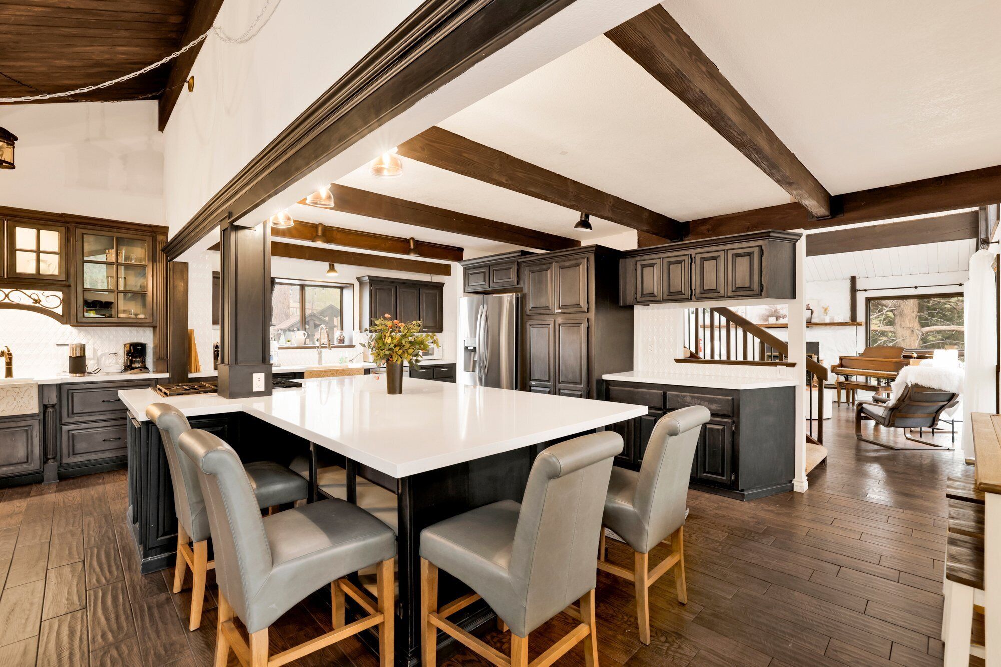 A spacious kitchen with dark wooden cabinets, a central island with chairs, and a view of the living area.