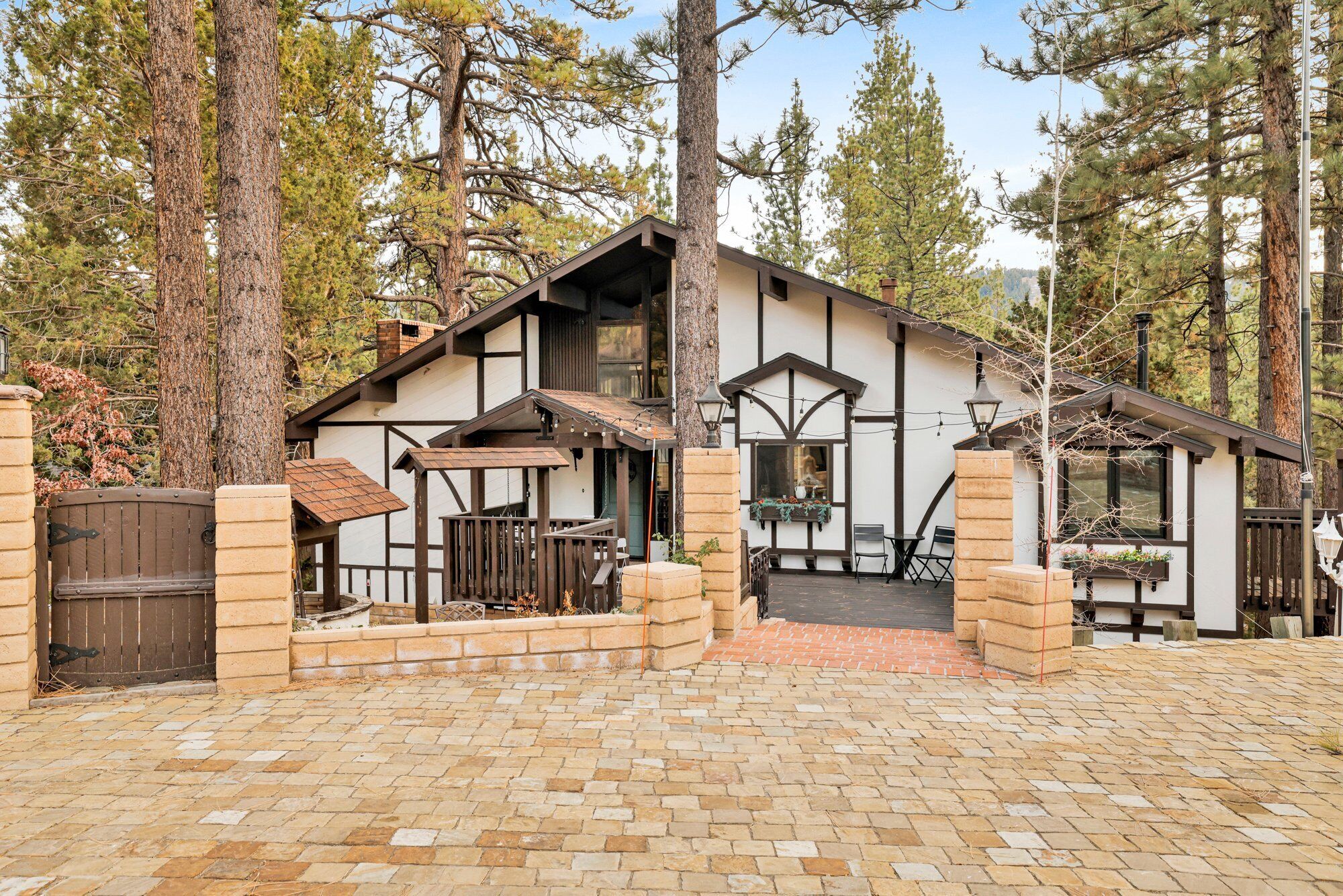A rustic cabin with a stone foundation, wooden deck, and a large window overlooking a forested area.