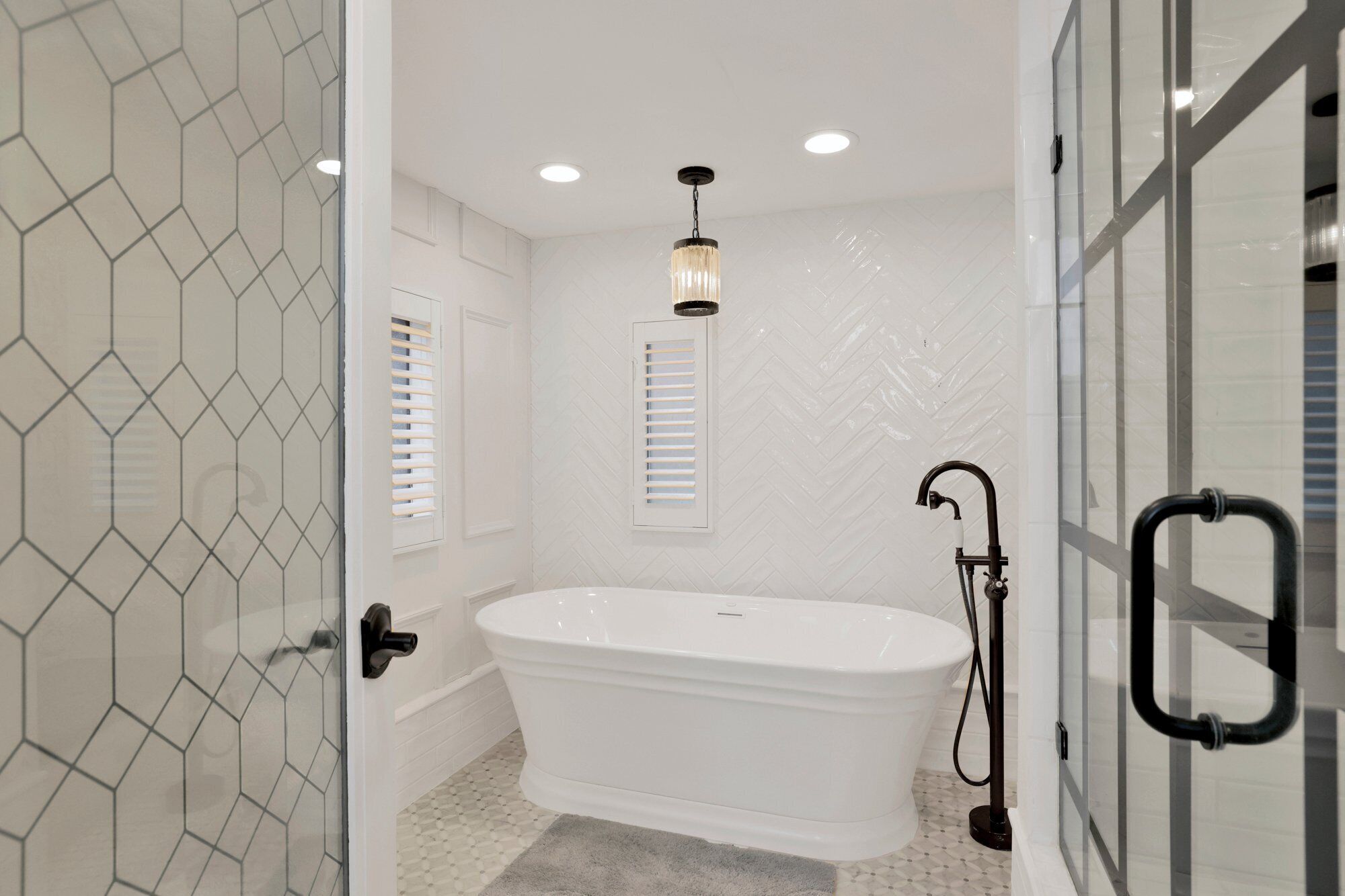 A modern bathroom with a freestanding bathtub, a glass shower enclosure, and a geometric tile backsplash.