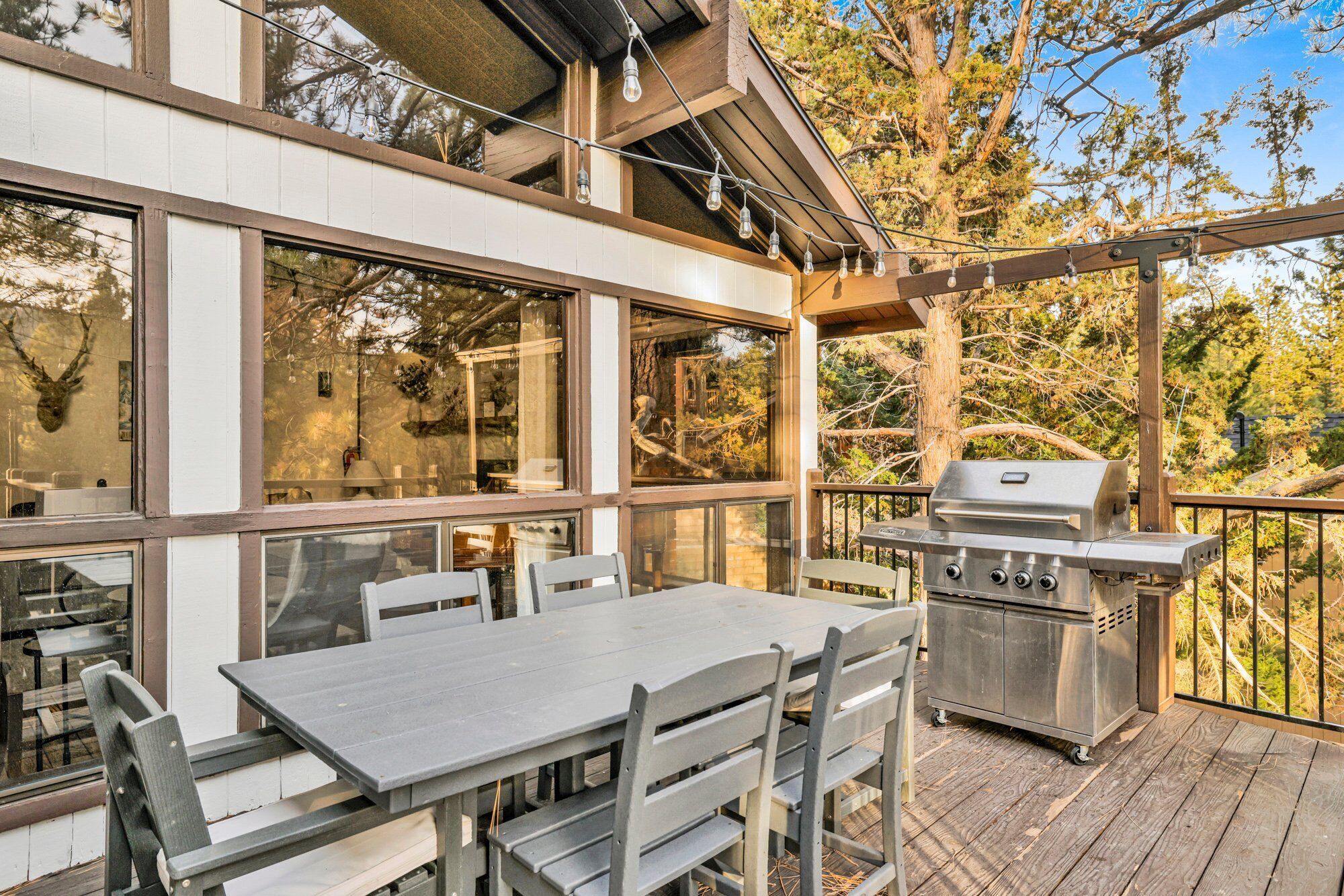 An outdoor patio with a table and chairs, a grill, and large windows overlooking trees.