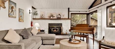 Una sala de estar acogedora con chimenea, un piano y un ventanal con vistas al exterior.
