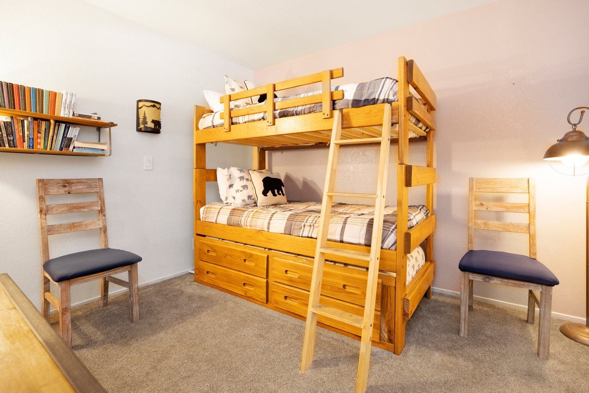A bunk bed with a ladder, two chairs, a bookshelf, and a lamp.