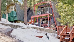 Une cabane à deux étages avec un balcon, entourée d’arbres et de neige.