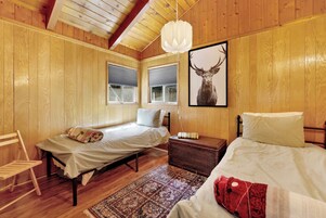 Un dormitorio de cabaña de madera con dos camas, un tapete tejido y un cuadro con un venado.