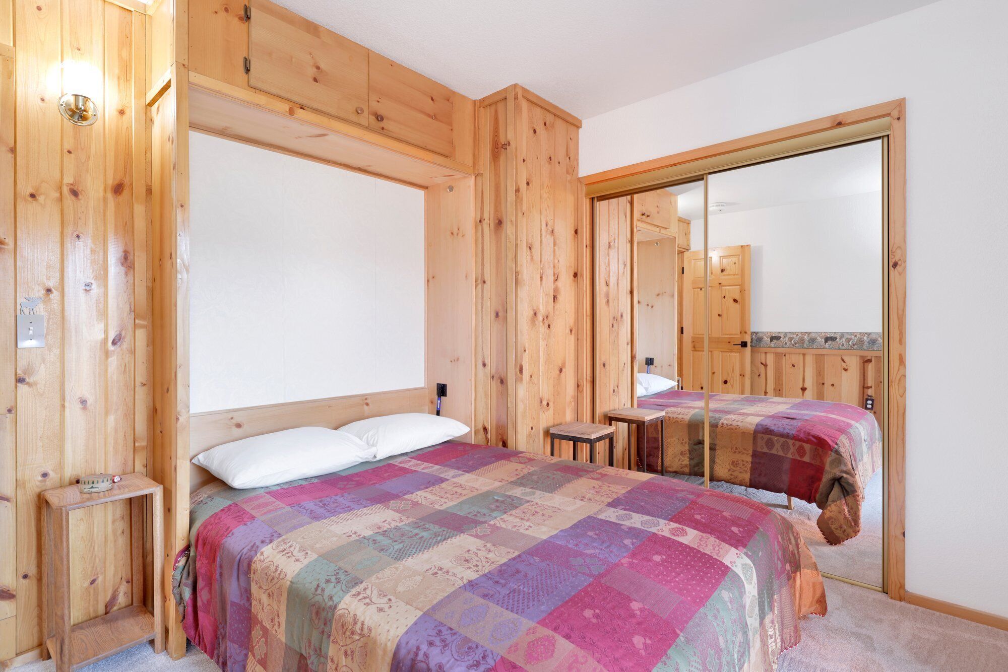 Ein Zimmer mit Holzboden, zwei Betten, einem kleinen Tisch und einem Spiegel.