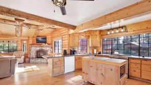 A log cabin interior with a stone fireplace, wooden cabinetry, and a large island with a stove. - THE Alps Lodge #2142 (Big Bear Lake)