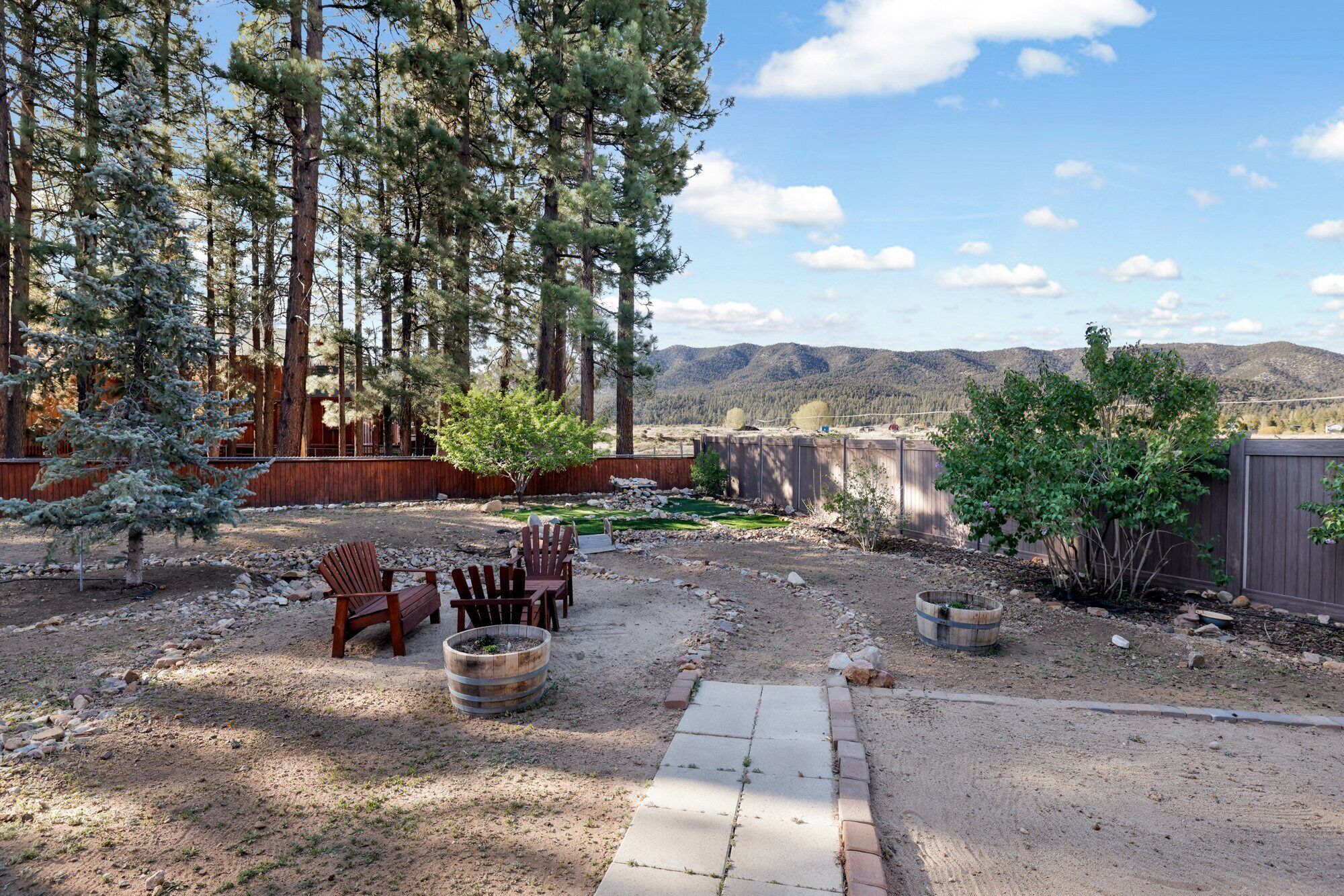 An outdoor patio area with a stone pathway, wooden chairs, and a fire pit.