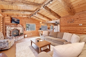 Interior acogedor de una cabaña de troncos con chimenea de piedra, muebles de madera y una zona de cocina.