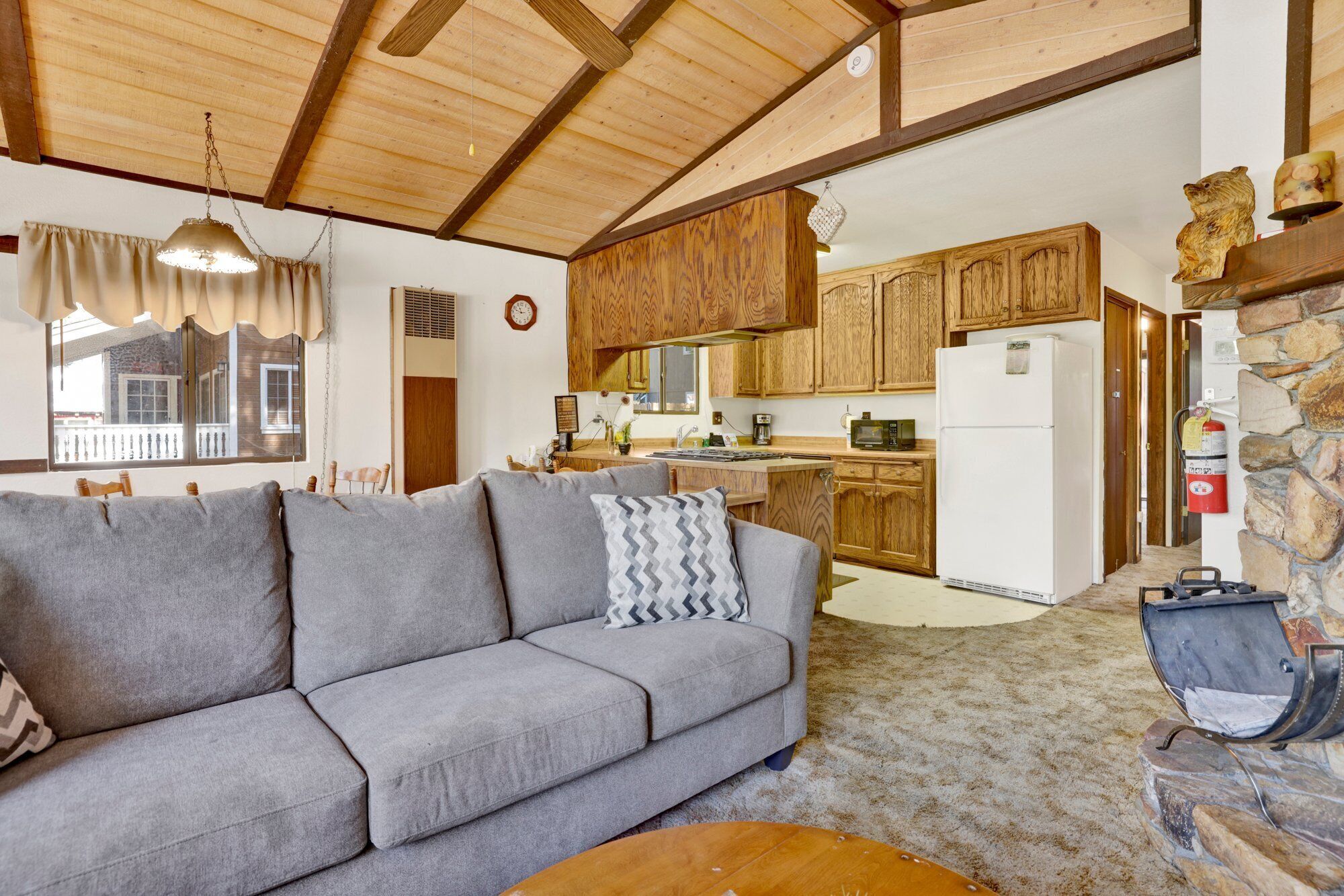 A cozy living room with a gray sofa, wooden ceiling beams, and a stone fireplace.