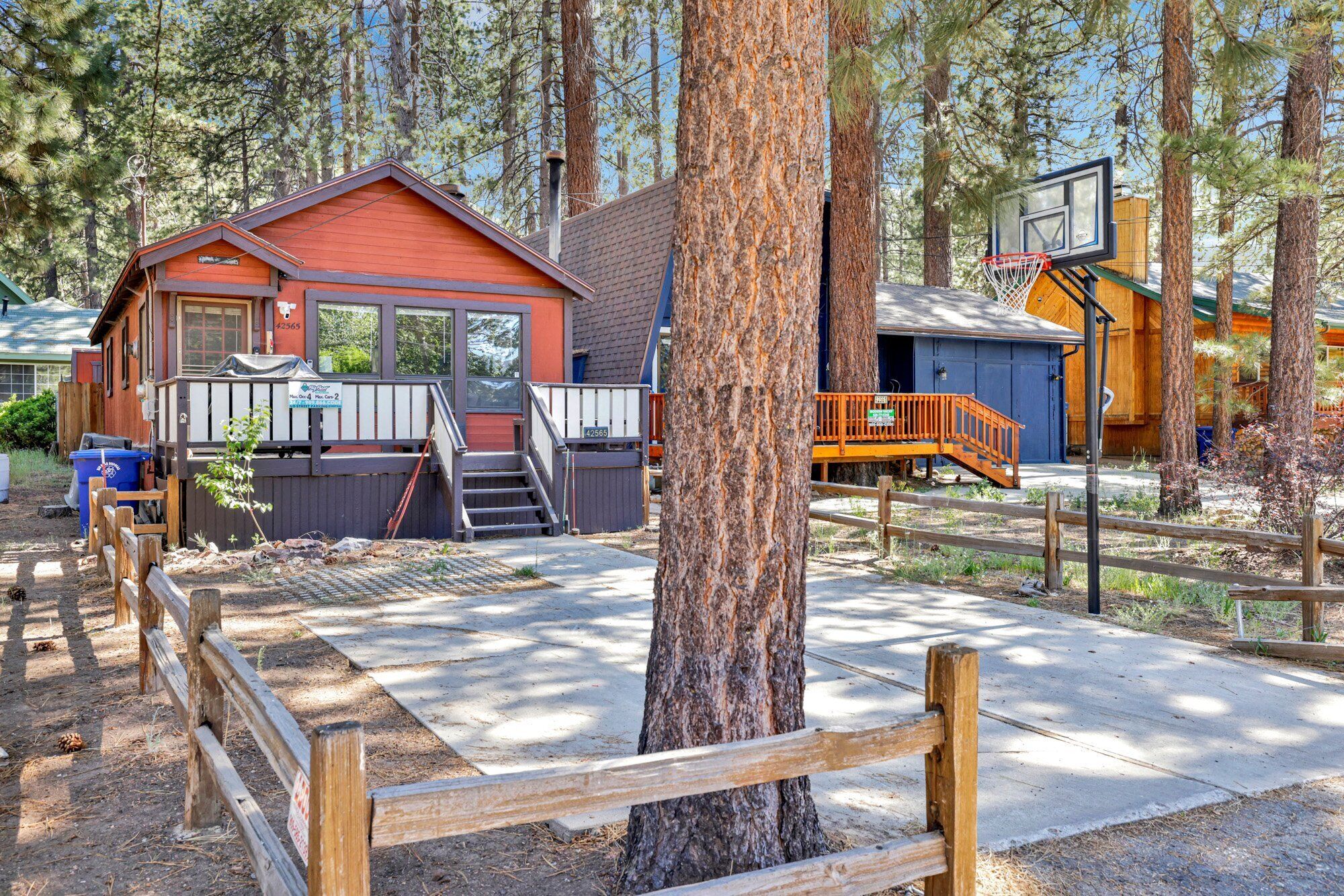 A cabin with a red exterior, a wooden deck, and a basketball hoop.