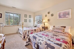 A bedroom with two beds, a window, a fan, and wall decorations. - Idle Hours INN #1945 (Big Bear City)