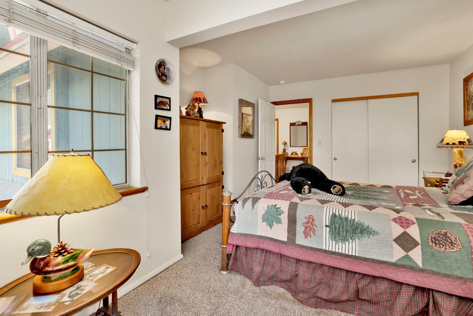 Un dormitorio con una cama, un armario de madera, un escritorio con lámpara y una ventana con persianas.