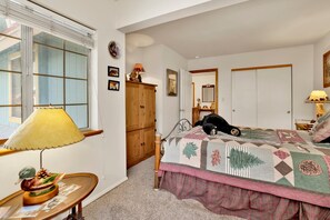 A bedroom with a bed, a wooden wardrobe, a window with blinds, a lamp, and a small table with a decorative item. - Idle Hours INN #1945 (Big Bear City)