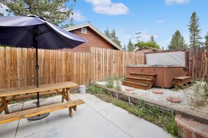 A backyard with a wooden picnic table, a hot tub, and a wooden fence. - Idle Hours INN #1945 (Big Bear City)