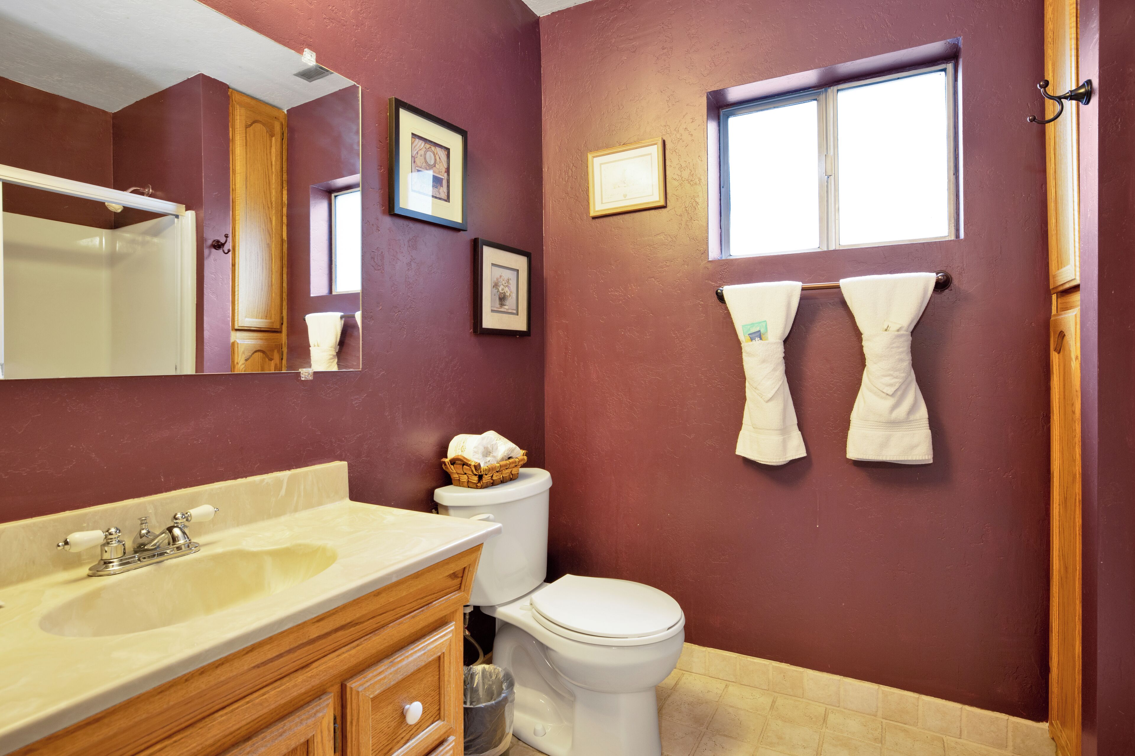 A bathroom with a beige sink, wooden vanity, white toilet, and two towels hanging on the wall.