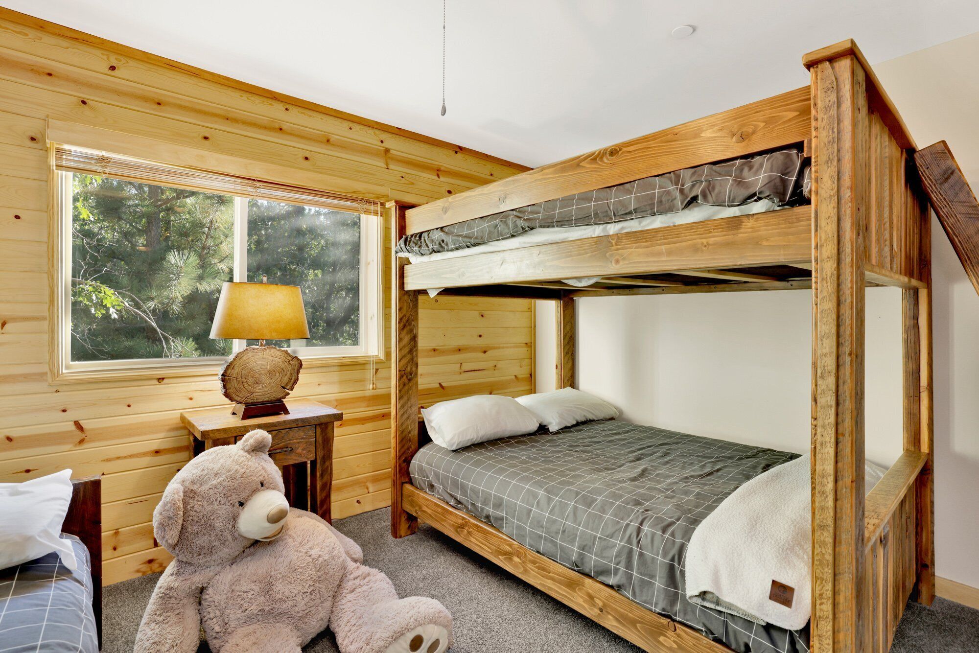 A bunk bed room with a window, a lamp, and a teddy bear.