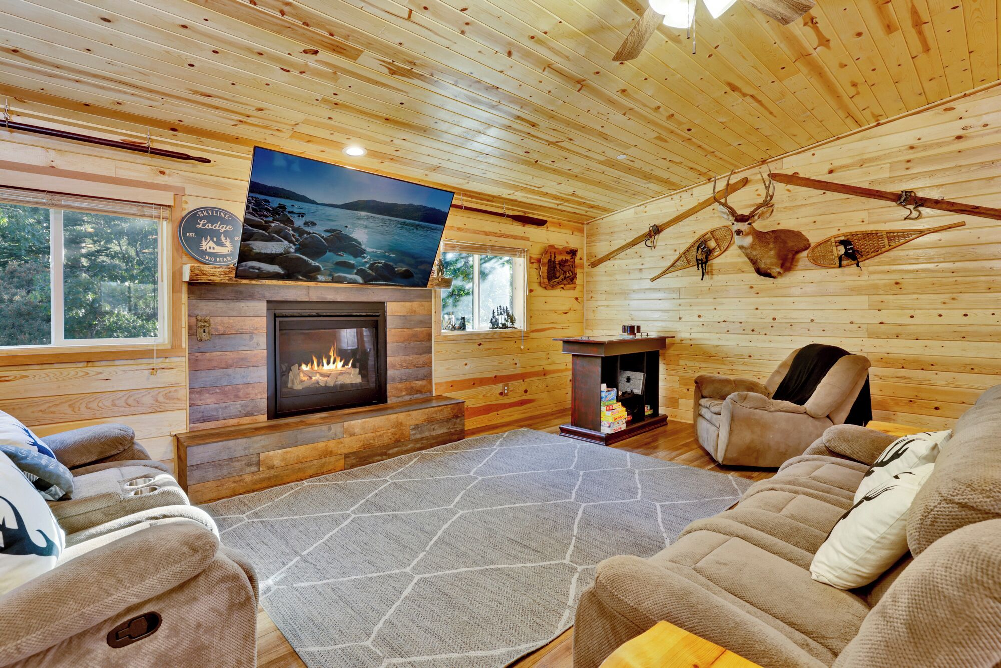 Interior acogedor de una cabaña con chimenea, paredes de madera y una televisión grande.