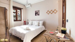 Un dormitorio con cama, una mesa de madera, una planta en maceta y una ventana con cortinas.