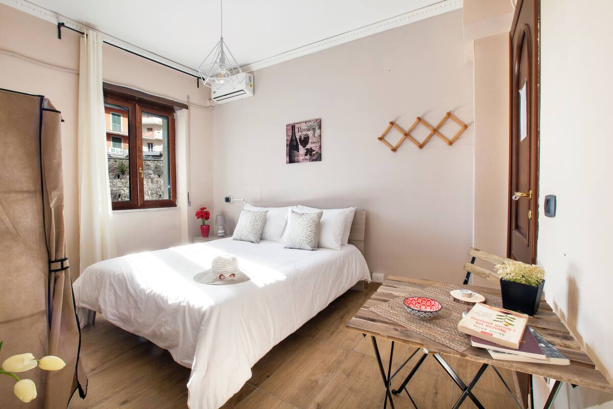 Una camera da letto con un letto, un tavolo di legno, una pianta in vaso e una finestra con tende.