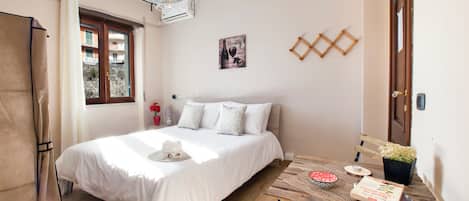 A bedroom with a bed, a wooden table, a potted plant, and a window with curtains.