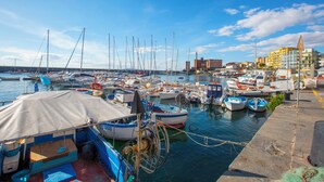 Un puerto deportivo con varias embarcaciones amarradas, un edificio de varios pisos y un cielo despejado.