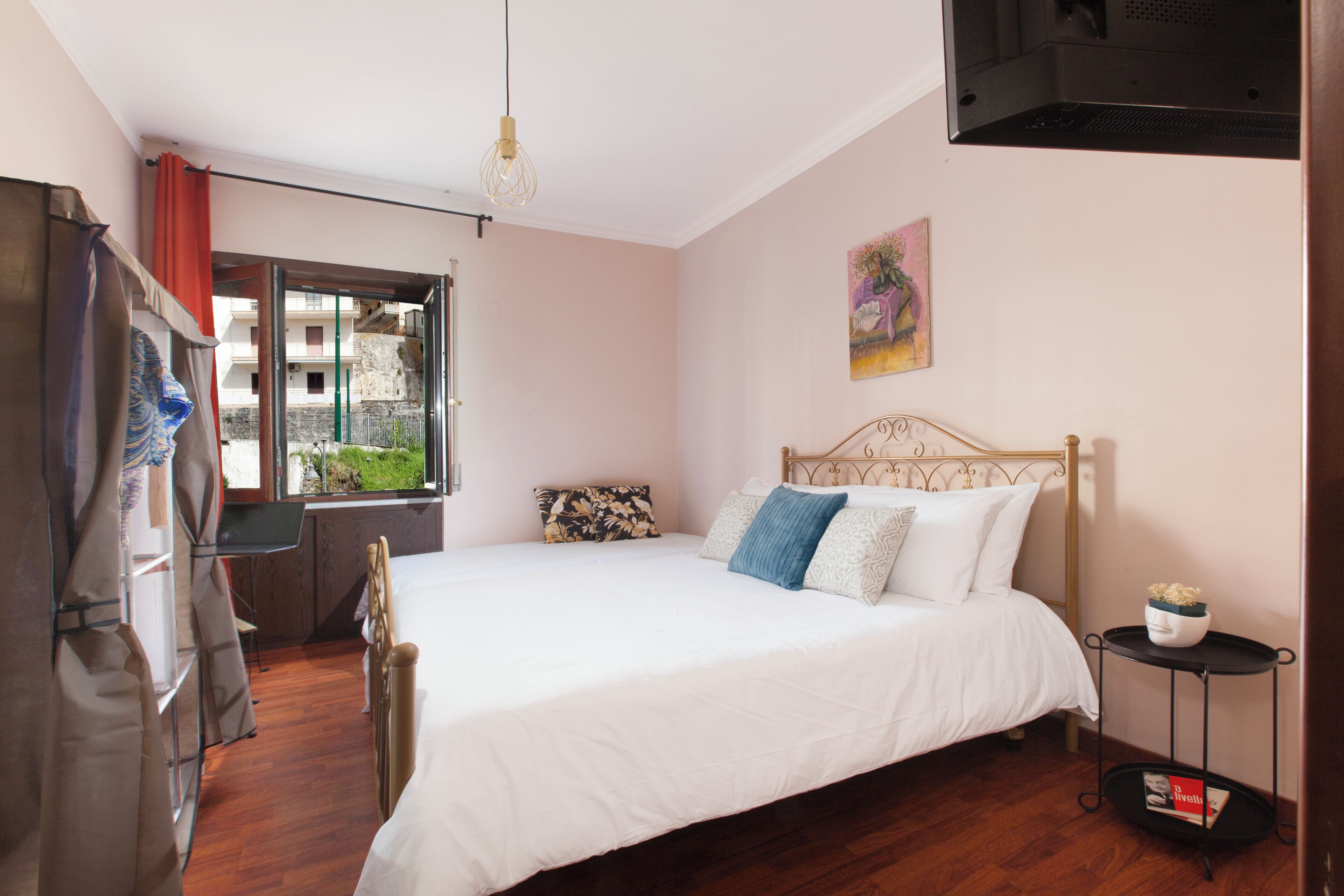 A bedroom with a bed, a desk, a window, and a painting on the wall.