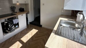 Eine kompakte Küche mit weißen Schränken, einem Backofen, einer Spüle und einem Fischgrätenboden.