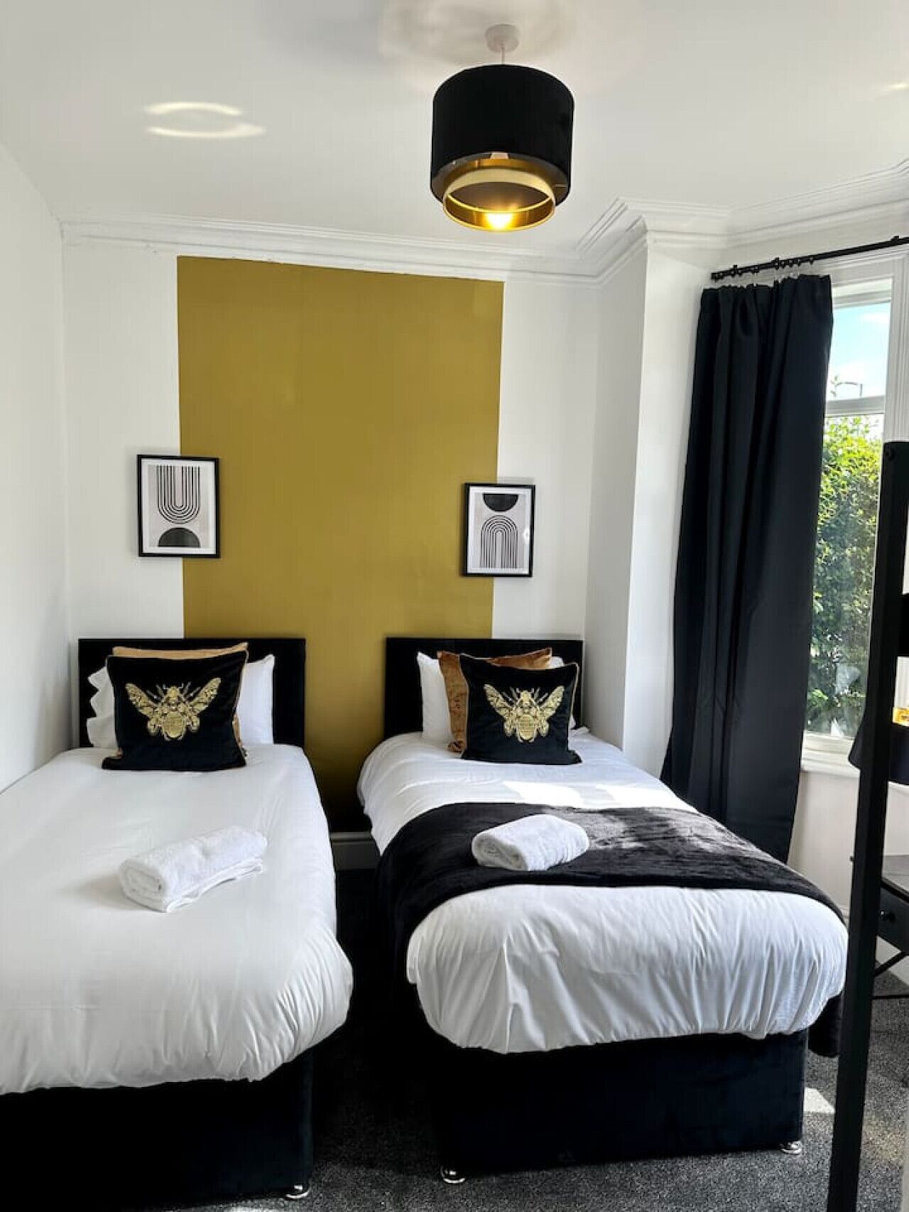 Une chambre d’hôtel avec deux lits, une décoration aux couleurs noir et or, et une grande fenêtre avec des rideaux.