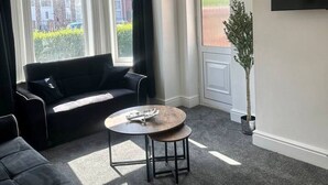 Ein modernes Wohnzimmer mit einer schwarzen Couch, einem runden Couchtisch und einem großen Fenster mit Vorhängen.